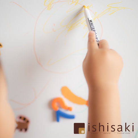 兒童手持白色畫筆在白色繪畫板上塗鴉，畫板上有黃色、橘色線條，下方有橘色、藍色磁性數字或字母，以及一個可愛的卡通造型磁鐵。