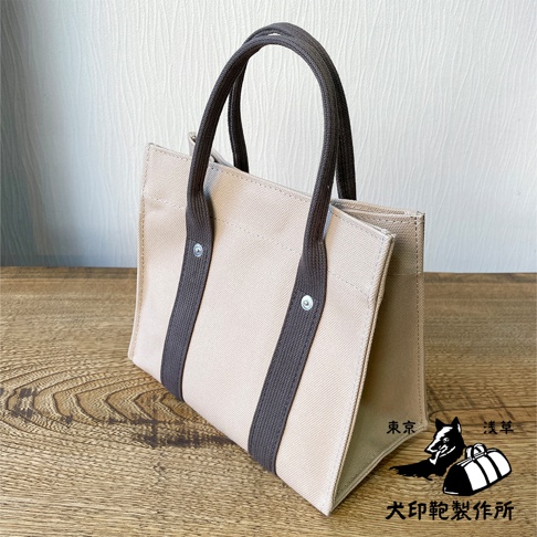 犬印純棉帆布迷你托特包，淺褐色帆布包身，深褐色提把及側邊裝飾條，以鈕扣固定，結構立體，風格簡約。