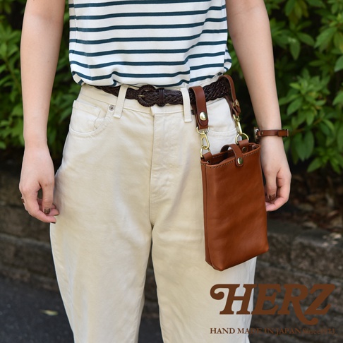 職人手作皮革兩用手機包，呈現棕褐色，以真皮材質製作，設計簡約，可掛於腰帶或作為斜背包使用。