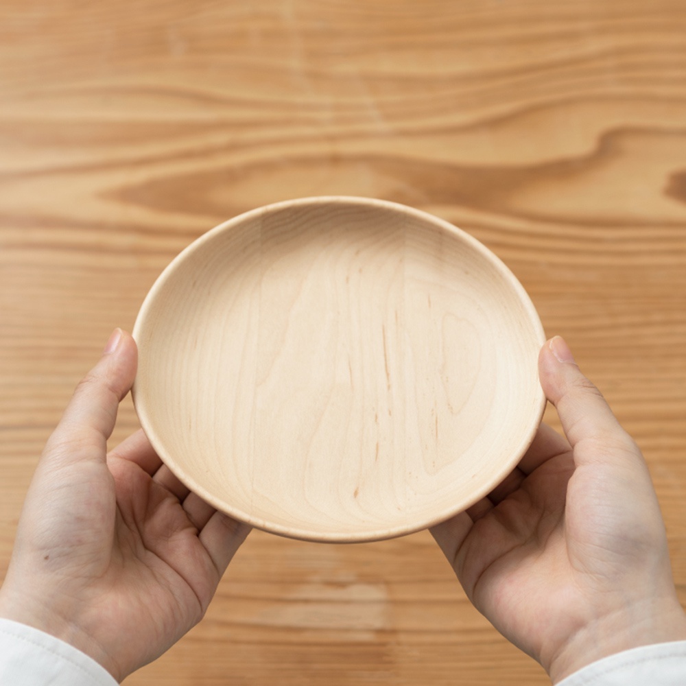 兩隻手捧著一個淺色的楓木盤，盤子呈現圓形，表面有細緻的木紋。