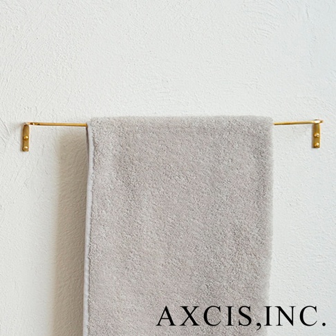 金黃色單桿黃銅毛巾架，以 L 型固定於白色牆面，掛有一條淺灰色毛巾。