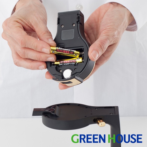 雙手正在將兩顆金色 AA 電池裝入黑色啤酒金泡機的電池槽，電池槽內有兩個金屬接觸點和一個圓形電池。機身為黑色塑膠，邊緣飾有金色線條。