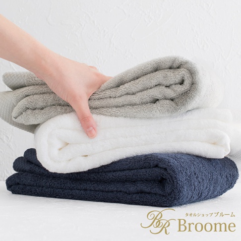 疊放的三條今治純棉長浴巾，分別為淺灰色、白色和海軍藍，手部觸碰頂部淺灰色浴巾，浴巾表面有細緻的菱紋織紋。