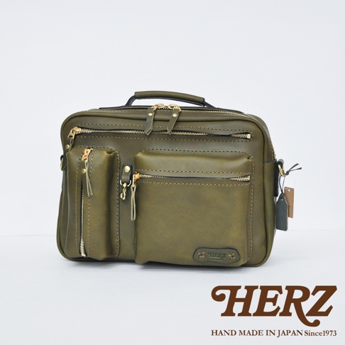 綠色皮革製成的多功能單肩包，設有頂部提把、多個拉鍊隔層和外袋，以及金色拉鍊和皮革飾帶。