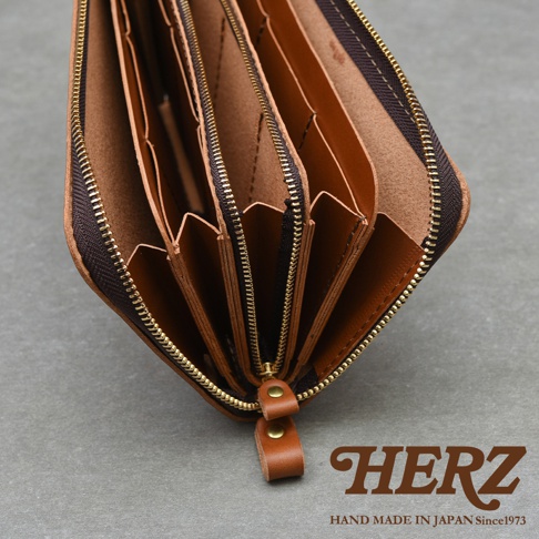 此為職人手作皮革Organ拉鍊長夾，展示其內部多層隔間與金色拉鍊細節，右下角印有HERZ品牌標誌及HAND MADE IN JAPAN Since1973字樣。