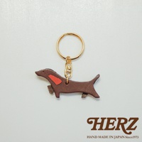 深棕色皮革製成的狗狗造型鑰匙圈，點綴紅色裝飾，搭配金色鑰匙環與掛鉤。