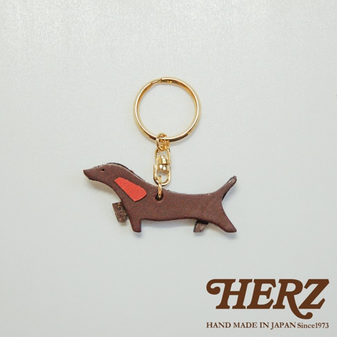 深棕色皮革製成的狗狗造型鑰匙圈，點綴紅色裝飾，搭配金色鑰匙環與掛鉤。