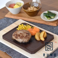 HAI減煙火山灰烤盤，長方形，深棕色，材質為火山灰陶。盤上盛有漢堡排、玉米粒、胡蘿蔔塊和馬鈴薯塊，整體呈現日式餐點風格。