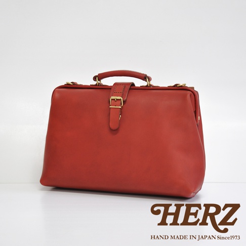 紅色皮革製成的職人手作軟式杜勒斯包，設有金色釦帶和提把。