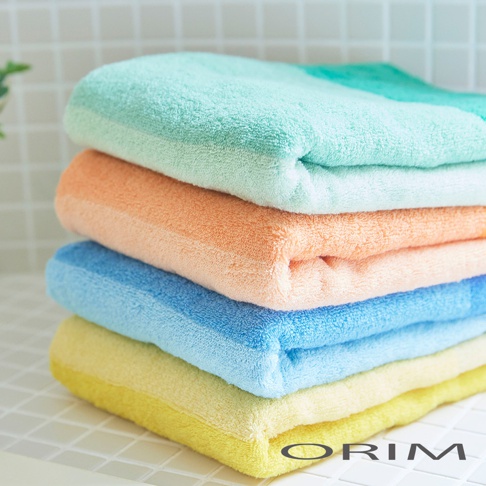 一疊四條柔軟的純棉毛巾，顏色由上至下分別為：薄荷綠、珊瑚橘、嬰兒藍、檸檬黃。毛巾質地蓬鬆，邊緣整齊。