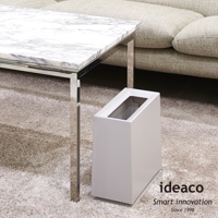 淺灰色方形垃圾桶，頂部斜面開口，置於客廳地毯上，搭配大理石紋桌面茶几。