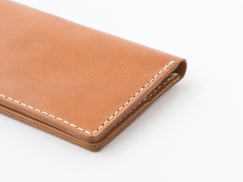 職人手作皮革簡約輕薄扁長夾，採用天然棕色皮革製成，邊緣以白色縫線裝飾，呈現細緻的工藝與簡潔的設計。