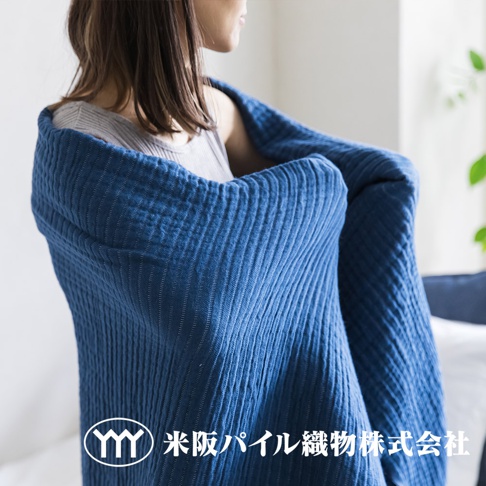 一位女性身披藍色三層紗輕透波紋四季毯，毯子有垂直的波紋紋理。