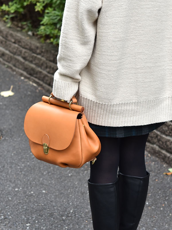 一個焦糖色皮革迷你後背包，配有頂部提把和金色金屬旋轉鎖扣。