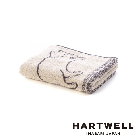 白色背景下放置著一條摺疊整齊的 Hartwell 今治午睡貓咪雙色毛巾，毛巾為米色與深灰色配色，表面飾有深灰色的貓咪剪影圖案，邊緣帶有細緻的織紋設計，呈現出柔軟舒適的質感。