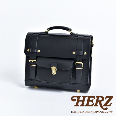 黑色皮革迷你後背包，學院風格設計，配有頂部提把、前置翻蓋口袋、金屬釦環與鉚釘裝飾，底部有金屬腳釘。