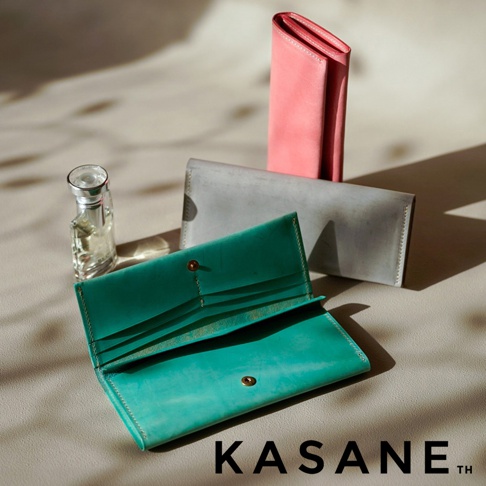 北海道KASANE職人手作義大利Sibilla皮革長夾，展示了綠色、灰色和粉紅色的皮革長夾，旁邊擺放著一瓶香水，圖片下方有KASANE品牌名稱。