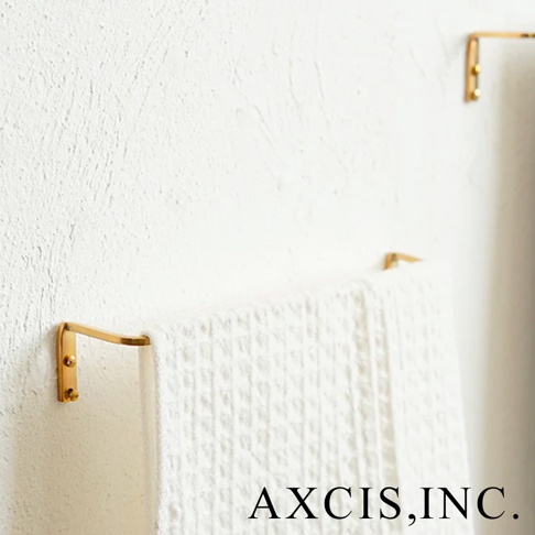 黃銅單桿毛巾架，表面光滑，金屬光澤，固定於白色紋理牆面，懸掛一條白色素面毛巾。