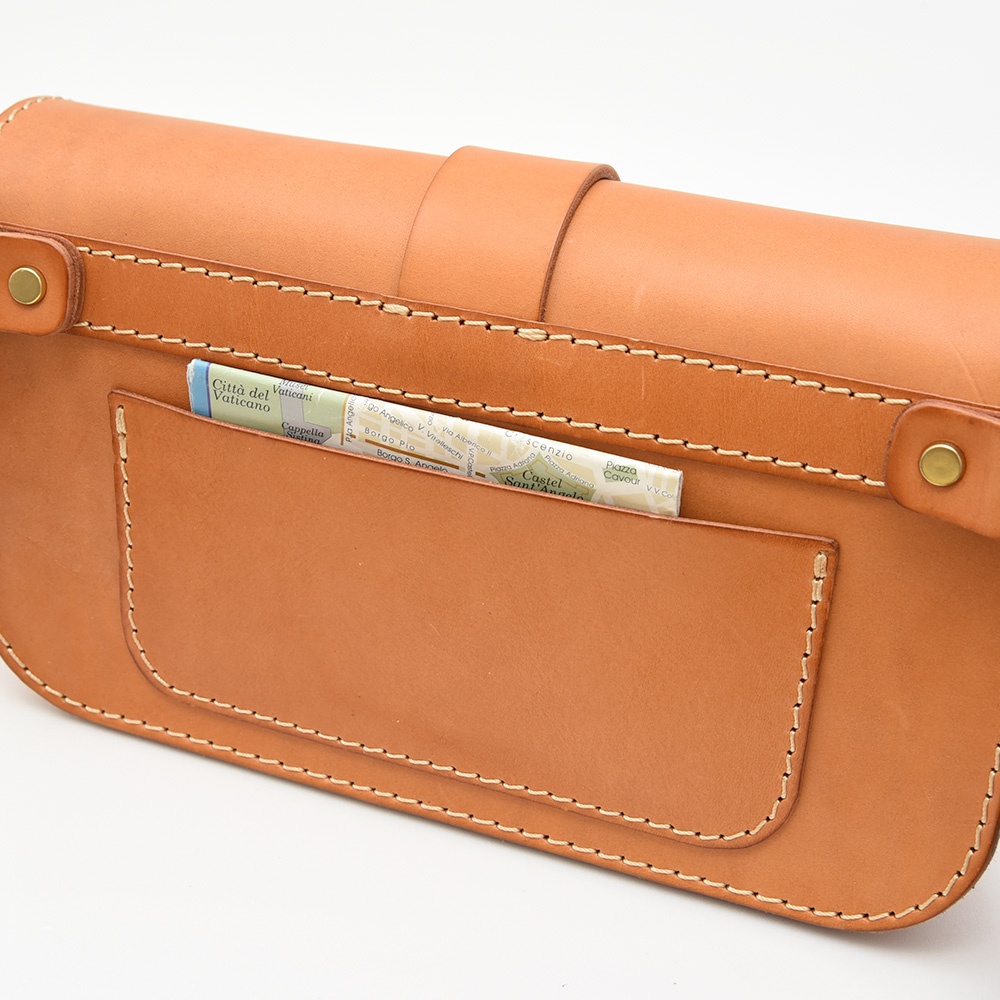 職人手作的經典斜背包，採用天然皮革材質，呈現原色棕。包款設計簡潔，設有單扣開闔，前方有一個插袋，露出部分地圖。縫線精緻，展現皮革的質感。