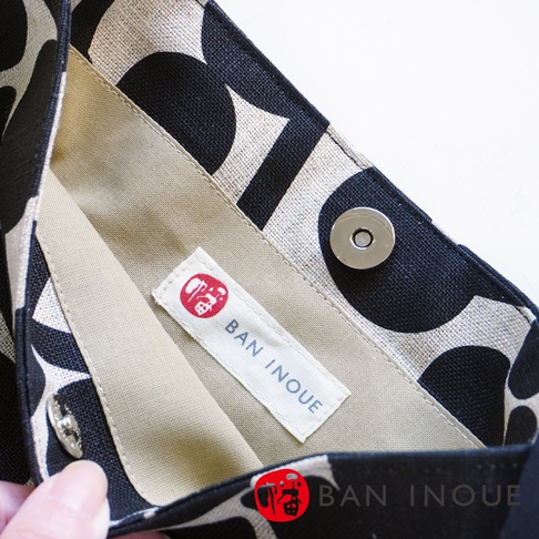 BAN INOUE 標籤和磁扣特寫，展現自然織紋麻布斜背包 (果實花紋) 的細節