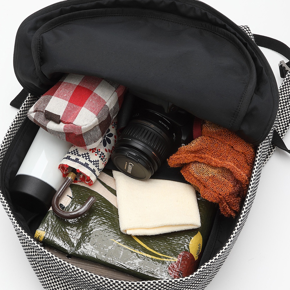 三河木綿刺子織後背包，黑色棋格圖案，內部裝有紅色格紋布包、白色保溫瓶、印花摺疊傘、相機、橘色毛巾及綠色包裝物品。