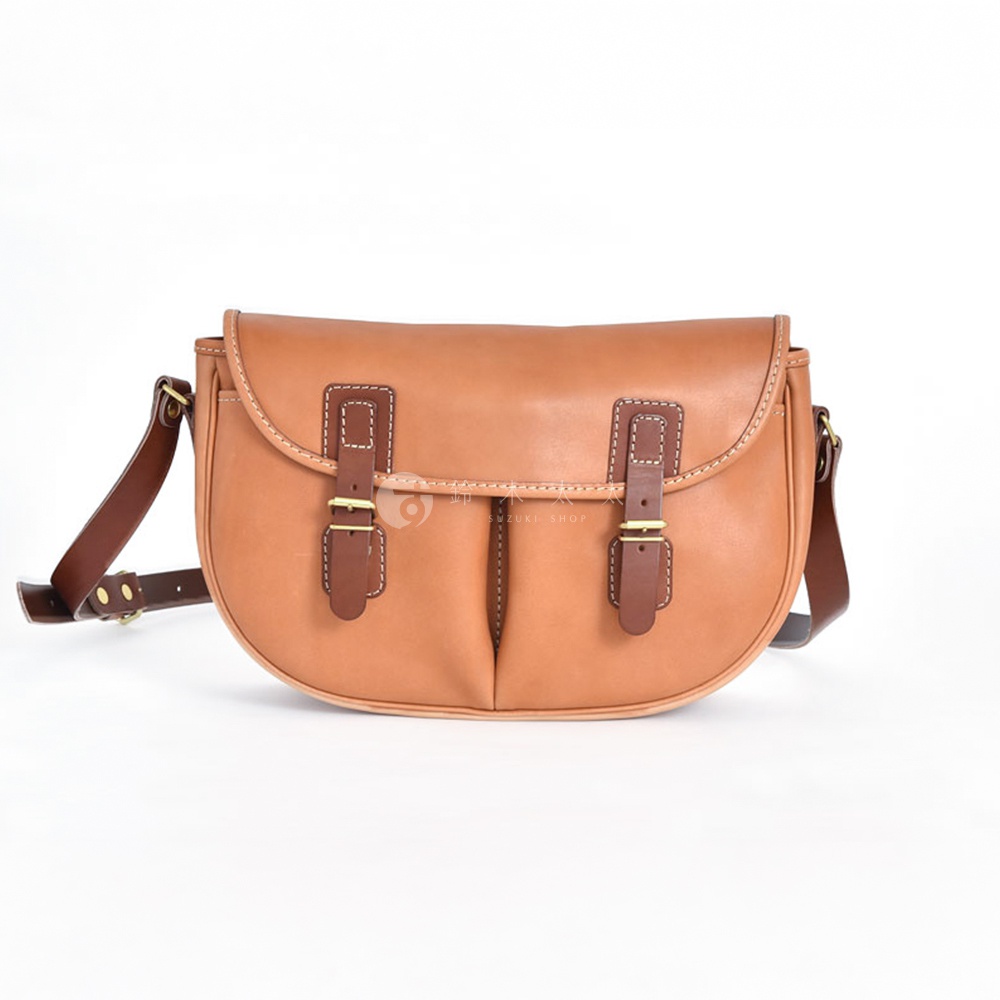 職人手作皮革傳統釣魚包，採用淺棕色皮革製作，配有深棕色皮革飾邊和兩條帶有黃銅搭扣的翻蓋。包身呈半圓形，有雙層前袋設計。