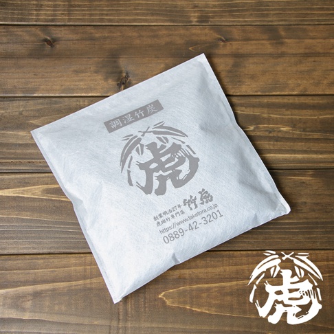 白色無紡布包裝的孟宗竹炭，印有灰色「虎」字圖案及日文說明，置於深色木紋背景上。