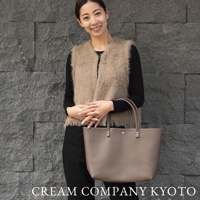 一位女性手持一個淺棕色皮革托特包，包包款式簡潔，配有雙提把。