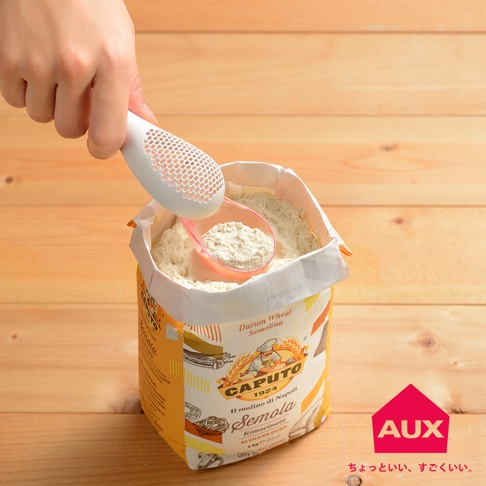 手持白色帶有網狀篩孔的調理專用撒粉器，正在從一包黃色包裝的CAPUTO Semola麵粉中舀取細緻的白色麵粉。