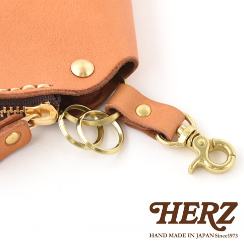 職人手作皮革鑰匙包，採用天然皮革材質，呈現淺棕色調。包款配有黃銅色拉鍊、按扣及掛鉤，並附有幾個金屬鑰匙圈。