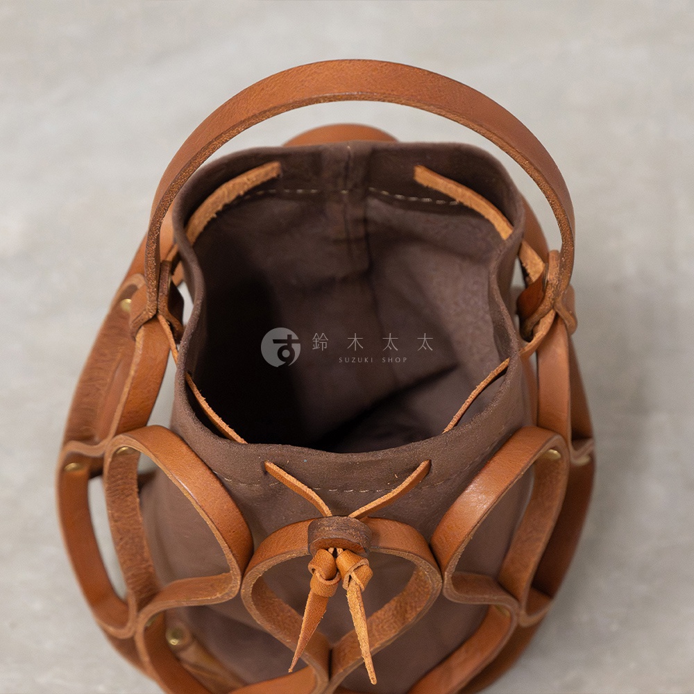 日本HERZ職人手作皮革Organ編織水桶包，近距離俯拍，展示棕色皮革編織框架與褐色帆布內袋，內袋上方有 SUZUKI SHOP 標誌。
