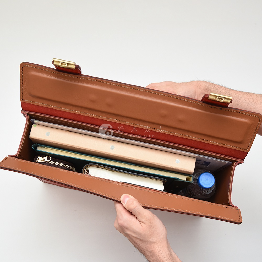 職人手作皮革兩用機師箱 BC-31-H，棕色皮革，內有書籍、筆記本、零錢包及一瓶水，箱蓋以金色金屬鎖扣固定。