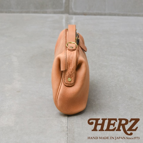 HERZ 品牌標誌，下方為「HAND MADE IN JAPAN Since1973」，左側為單肩包的側面視角，展示其皮革材質和鎖孔式的設計。