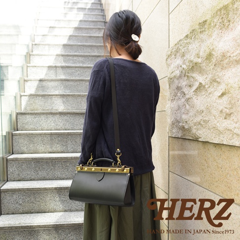 一位女士斜背一個黑色皮革復古口金兩用手提包，包包上有金色金屬配件和提把，整體呈現簡潔的設計風格。