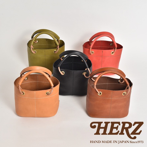五款不同顏色的職人手作皮革加厚提把大開口午餐袋，分別為綠色、紅色、黑色、淺棕色及深棕色，皆採用皮革材質，側邊有縫線及金屬孔設計，風格簡約。