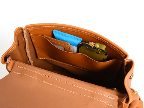 職人手作皮革屋瓦風經典雙扣後背包內部，展示棕色皮革內袋，內有藍色包裝物、卡片夾及綠色皮革零錢包。