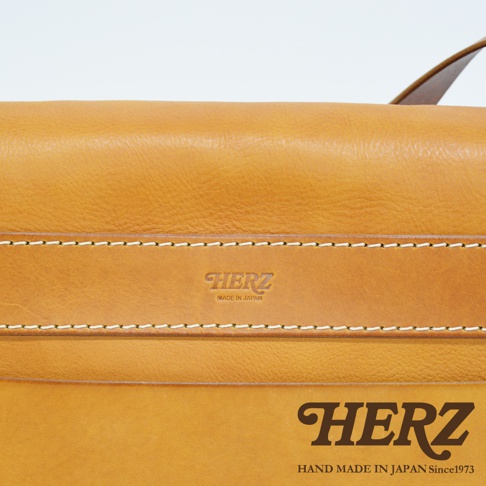 淺棕色皮革復古翻蓋郵差包，帶有品牌壓紋及精緻縫線，標示「MADE IN JAPAN」與「HAND MADE IN JAPAN Since1973」。