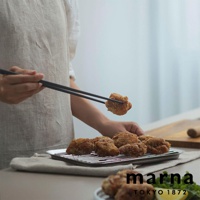 主體為炸雞塊，其中一塊正被黑色筷子夾起，下方盤子裡也擺放著多塊炸雞塊，圖片右下角印有「marna TOKYO 1872」的文字。