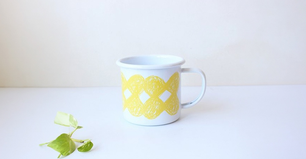 白色琺瑯馬克杯，杯身印有黃色交織的幾何圖案，附有白色把手。