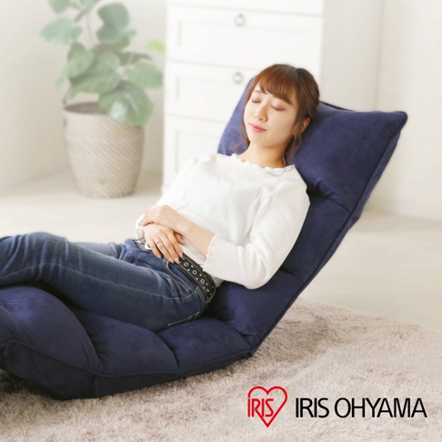 一位年輕女性在明亮的室內環境中，舒適地斜躺在深藍色的IRIS OHYAMA多段式紓壓單人沙發床上閉目休息，沙發床採柔軟絨面材質，下方鋪有淺灰色長毛地毯。