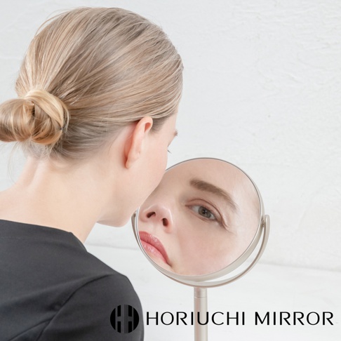 一位女性正望向香檳金色桌上型化妝圓鏡，鏡中映出她的臉部特寫，顯示 3 倍放大效果。