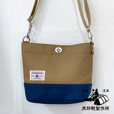 犬印純綿帆布雙色迷你側背包，上半部為卡其色，下半部為海軍藍，配有銀色轉鎖和可調節的帆布肩帶，左側有品牌標籤。