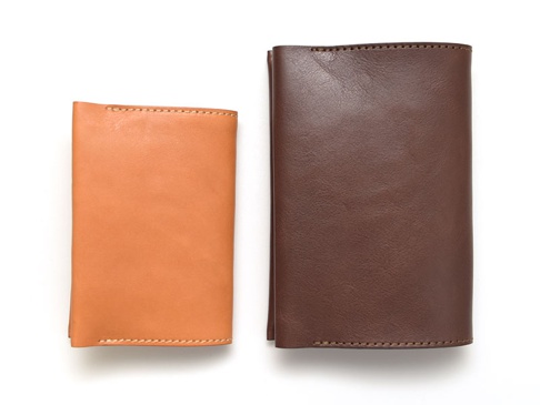 兩個職人手作皮革翻蓋記事本書套，一個為淺棕色，另一個為深棕色，皆為皮革材質，有縫線裝飾。