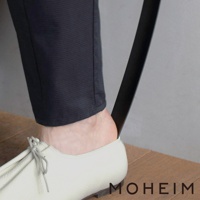 一隻腳穿著白色皮革鞋，鞋拔（黑色，長條形）插入鞋後跟，協助穿鞋。