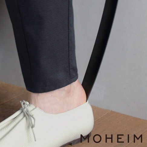 一隻腳穿著白色皮革鞋，鞋拔（黑色，長條形）插入鞋後跟，協助穿鞋。