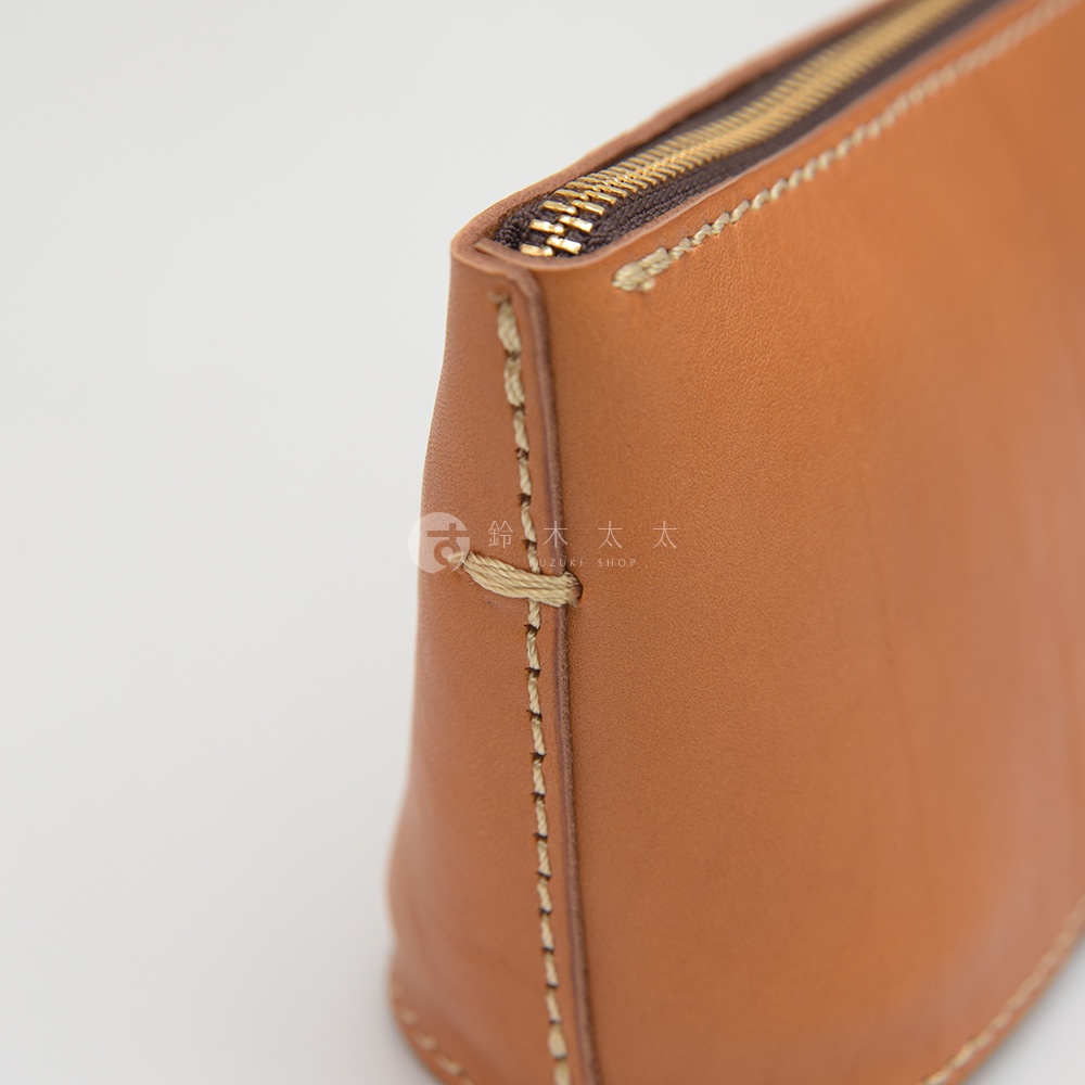 職人手作皮革三角收納包，採用淺棕色皮革，搭配金色拉鍊。包身以手工縫線拼接，展現細膩質感。
