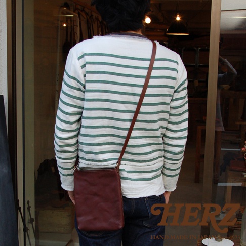 職人手作皮革Organ肩背小方包 G-26 L，深棕色皮革，簡約方型設計，搭配細長肩帶，由模特兒斜肩背於身後。