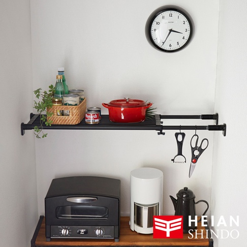 黑桿伸縮置物架，附有兩個層架，上方層架擺放紅色鑄鐵鍋、藤編籃裝有瓶罐和植物，下方懸掛著削皮器和剪刀。