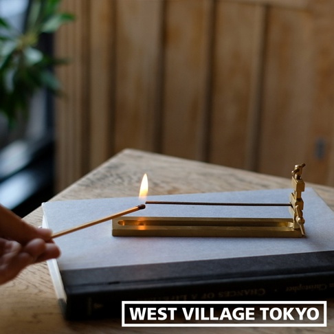 黃銅夾式水平線香架，夾持一根線香，線香一端點燃，散發火焰。