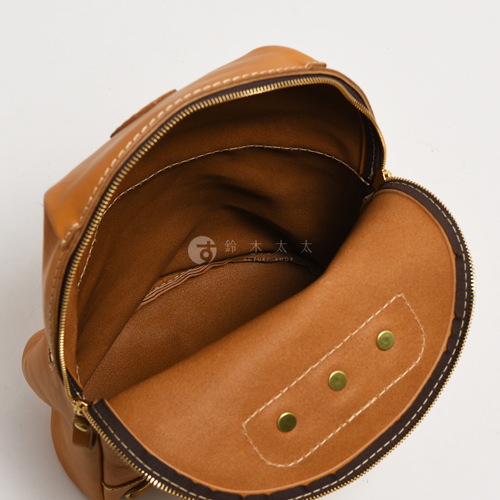 職人手作皮革大開口圓角後背包，展示棕色皮革材質，內部空間寬敞，設有拉鍊開合及銅扣裝飾，縫線清晰。